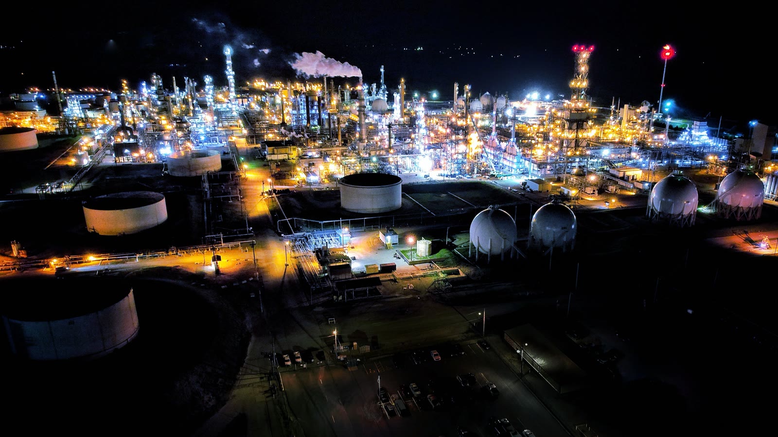 Illustrative night aerial view of a refinery complex and connected industrial infrastructure.