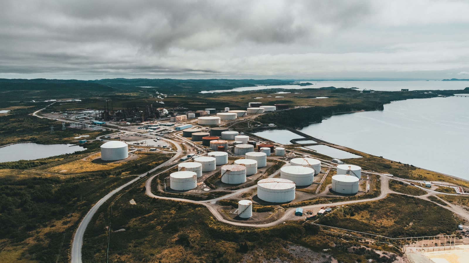 Illustrative aerial view of waterfront storage tanks and industrial port infrastructure.