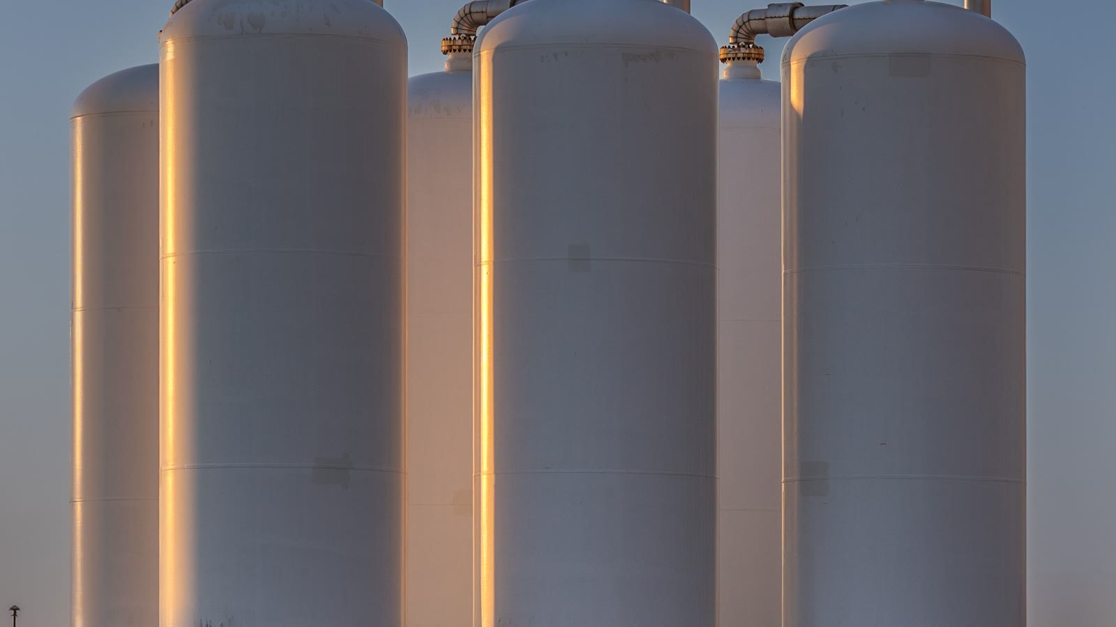 Illustrative sunset view of storage tanks and pipework in Rotterdam’s Botlek industrial area.