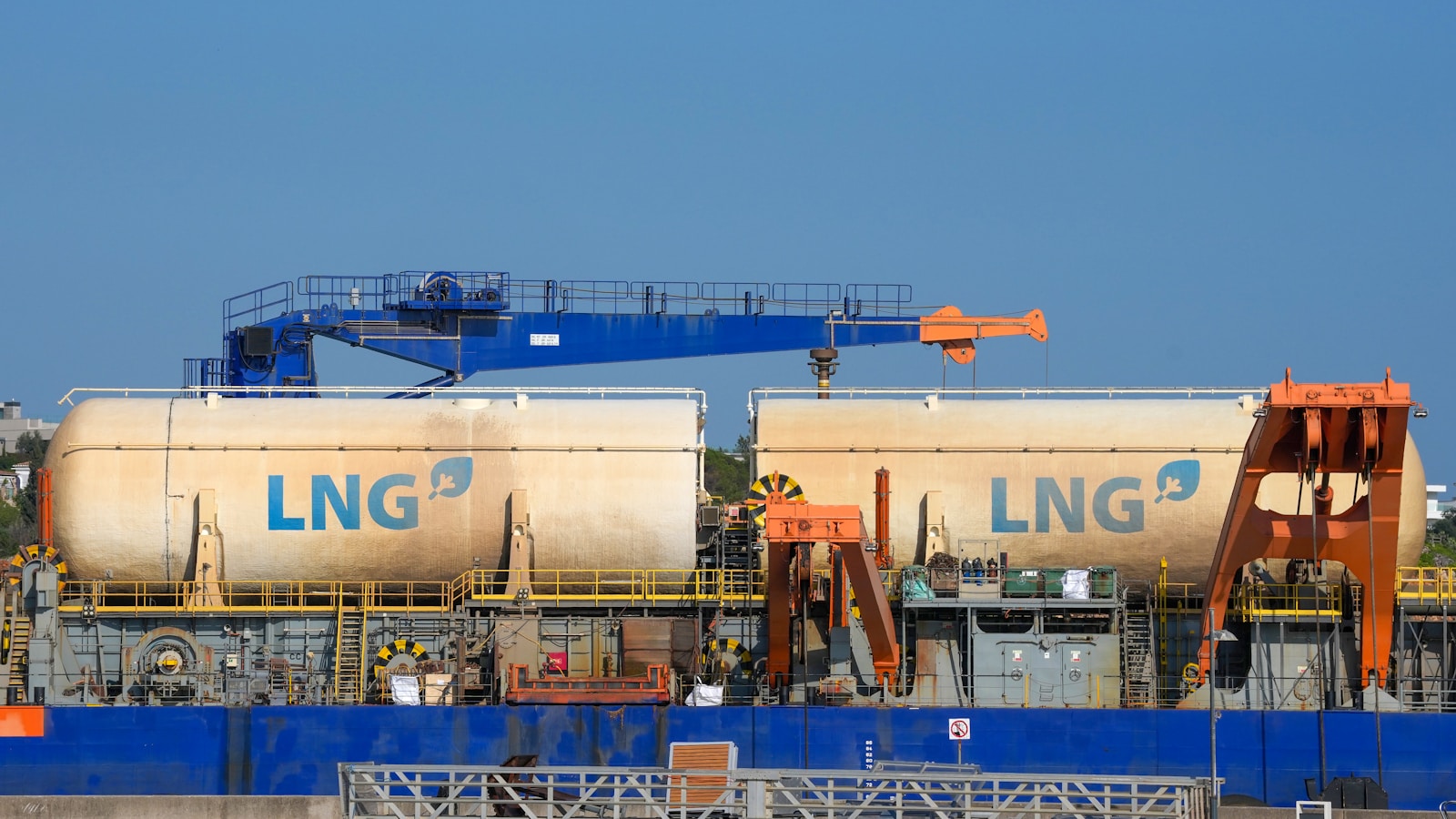 Illustrative LNG tanks on a barge beside port cranes.
