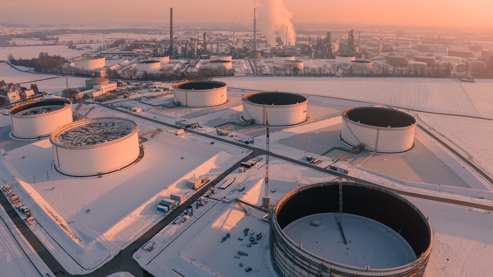 Illustrative aerial view of industrial tanks and refinery infrastructure at sunrise.