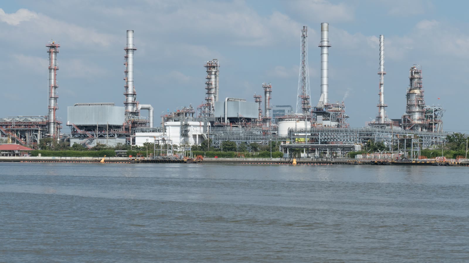 Illustrative waterfront oil refinery and storage infrastructure under cloudy skies.