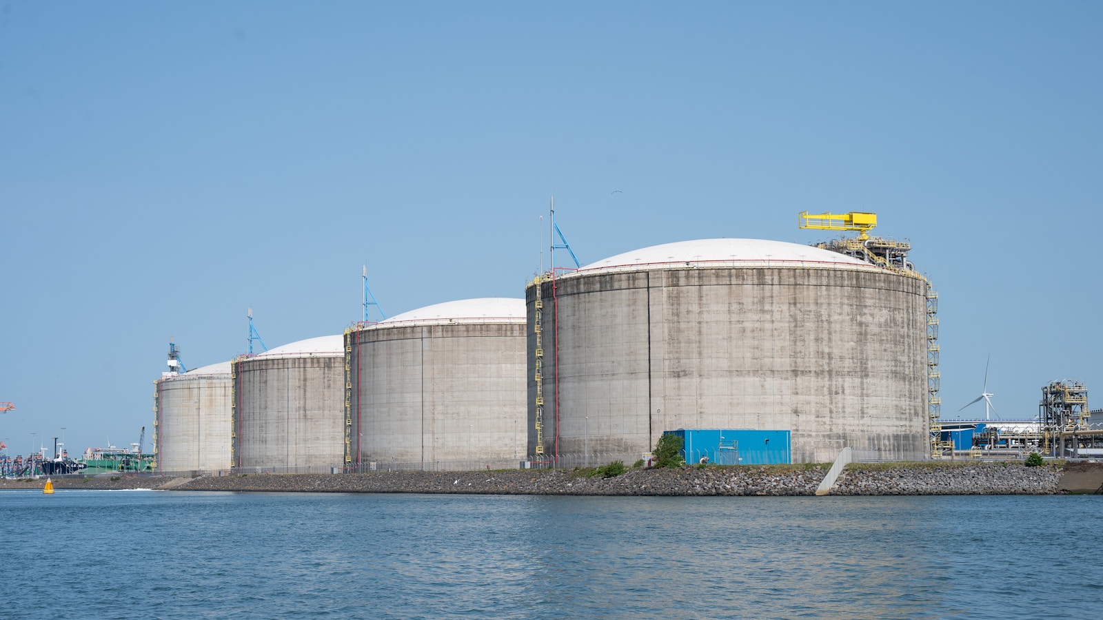 Illustrative waterside view of industrial storage tanks and energy infrastructure.